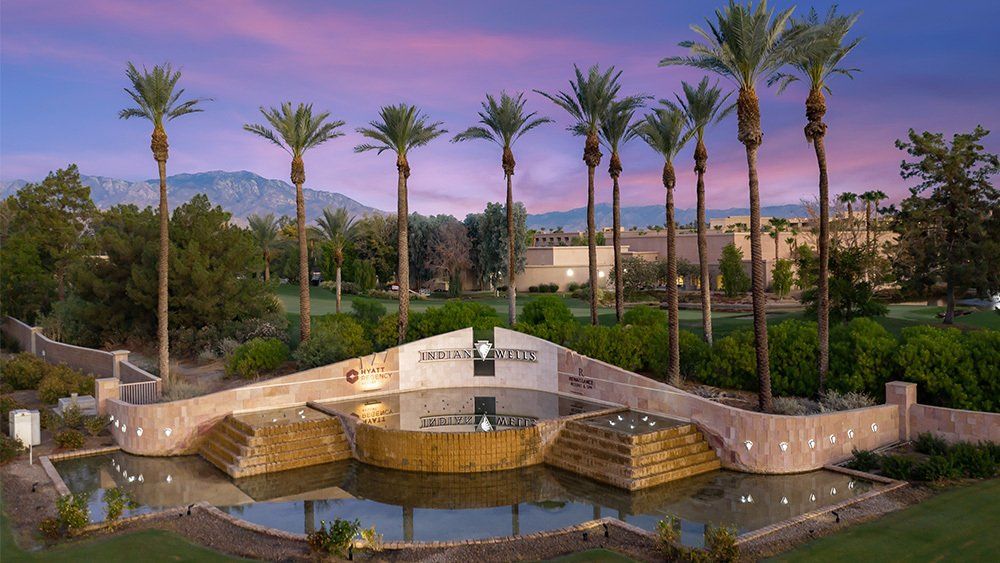 Palm-lined resort entrance with stone fountain and reflecting pool at sunset