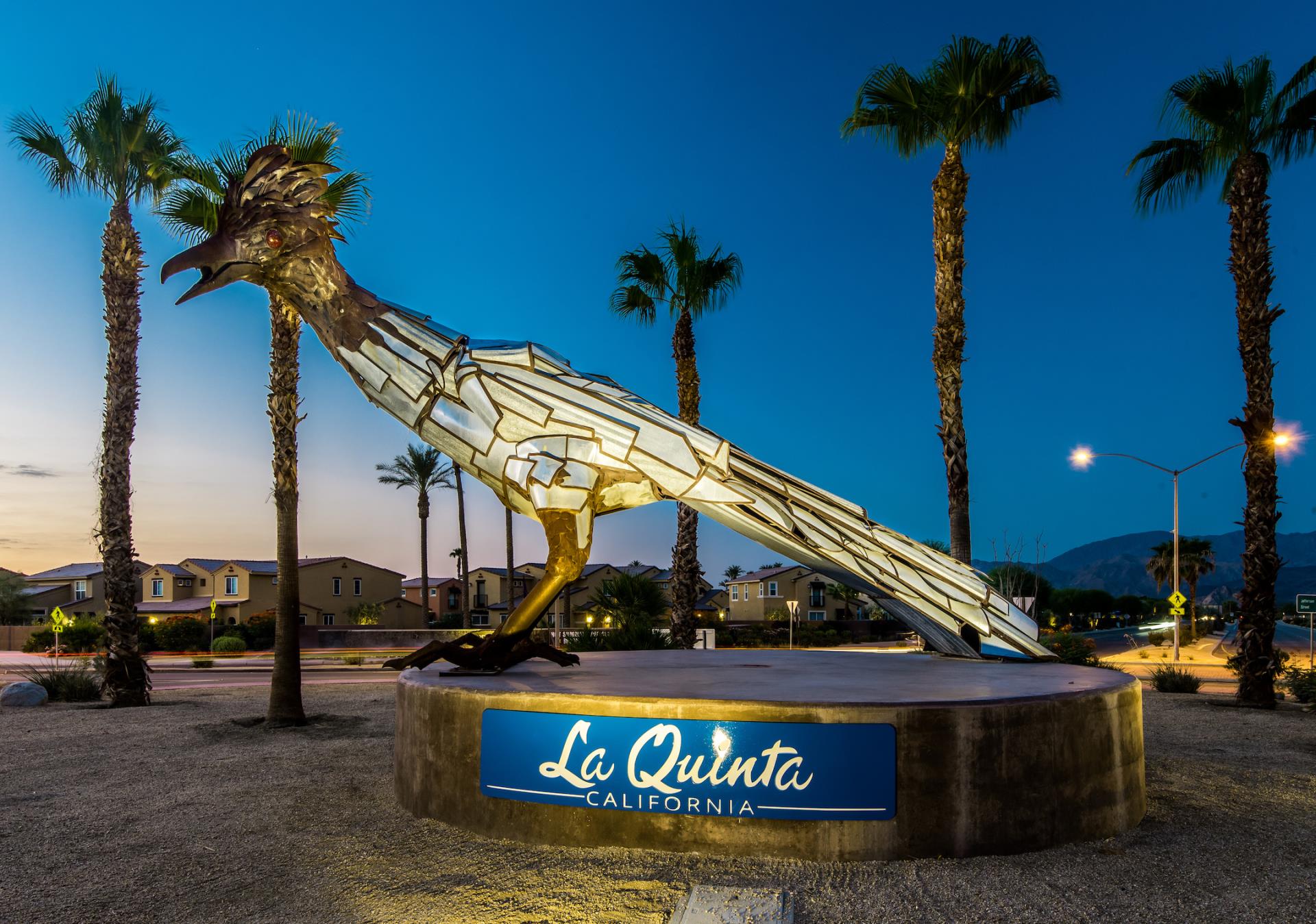 La Quinta resort sign with a large skeletal fish sculpture at dusk, palm trees and mountains behind