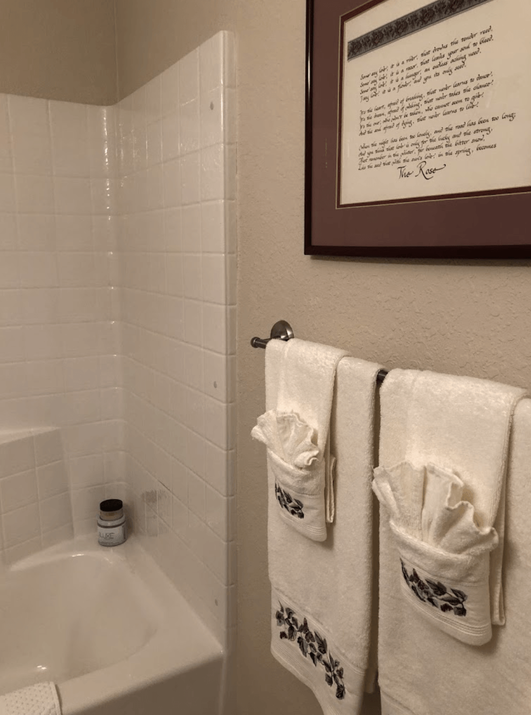 Bathroom with tub, white tile shower, and two white towel sets on wall hooks.