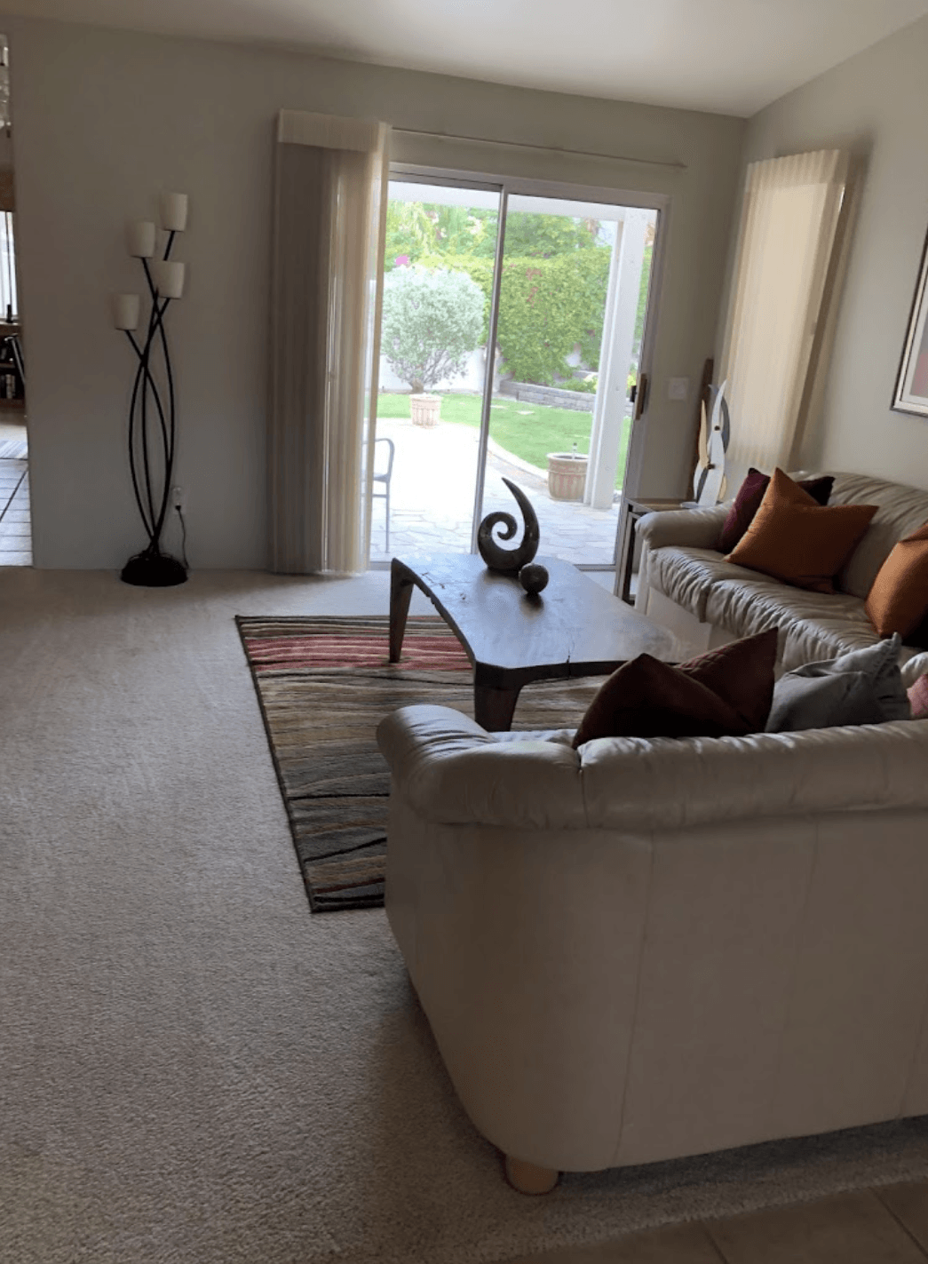 Bright living room with beige sofas, coffee table, rug, and sliding glass doors to a green yard.