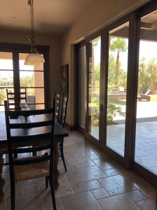 Dining room with dark table and chairs beside large glass doors overlooking a sunny patio and pool