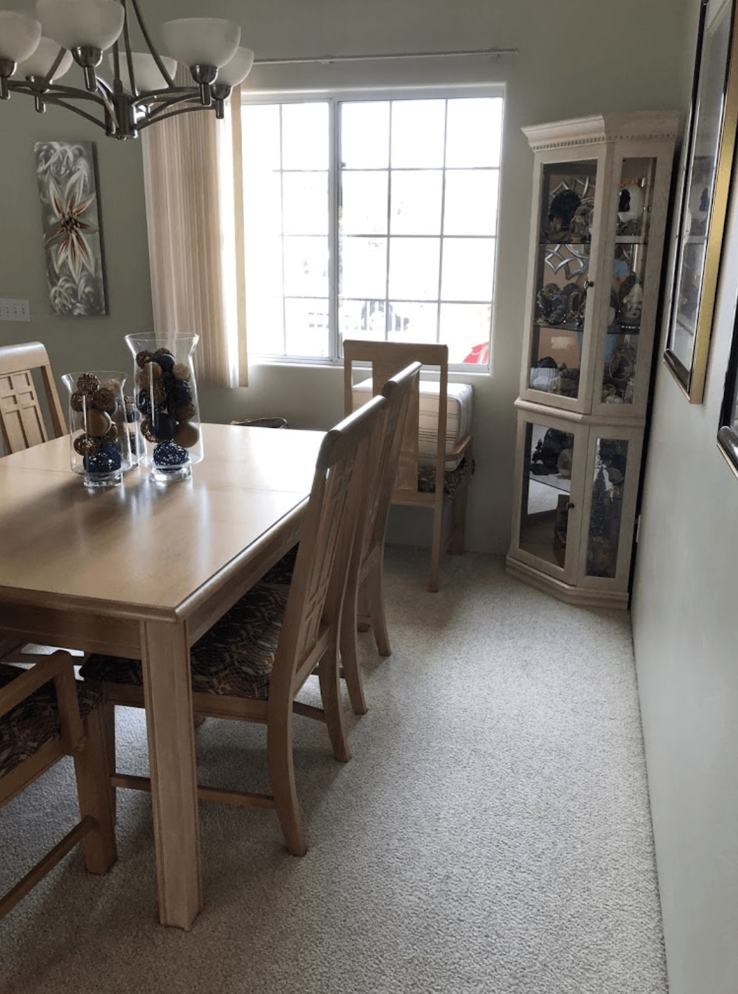 Dining room with wooden table, chairs, cabinet, and a window letting in daylight.