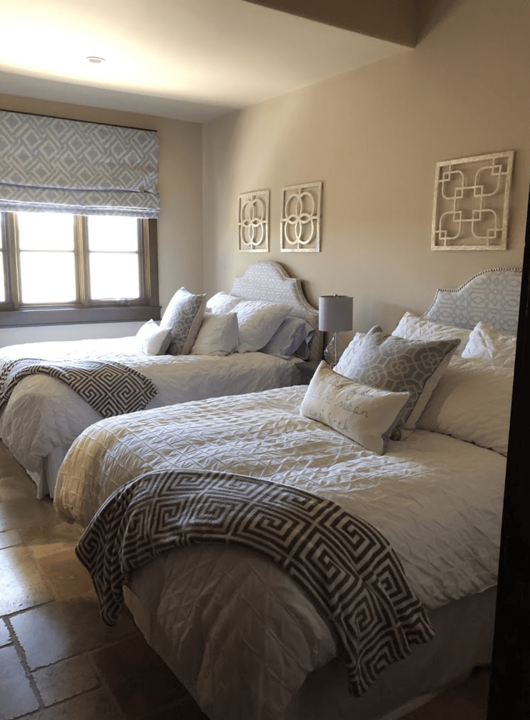 Three neatly made twin beds in a bright hotel room with a window and wall art