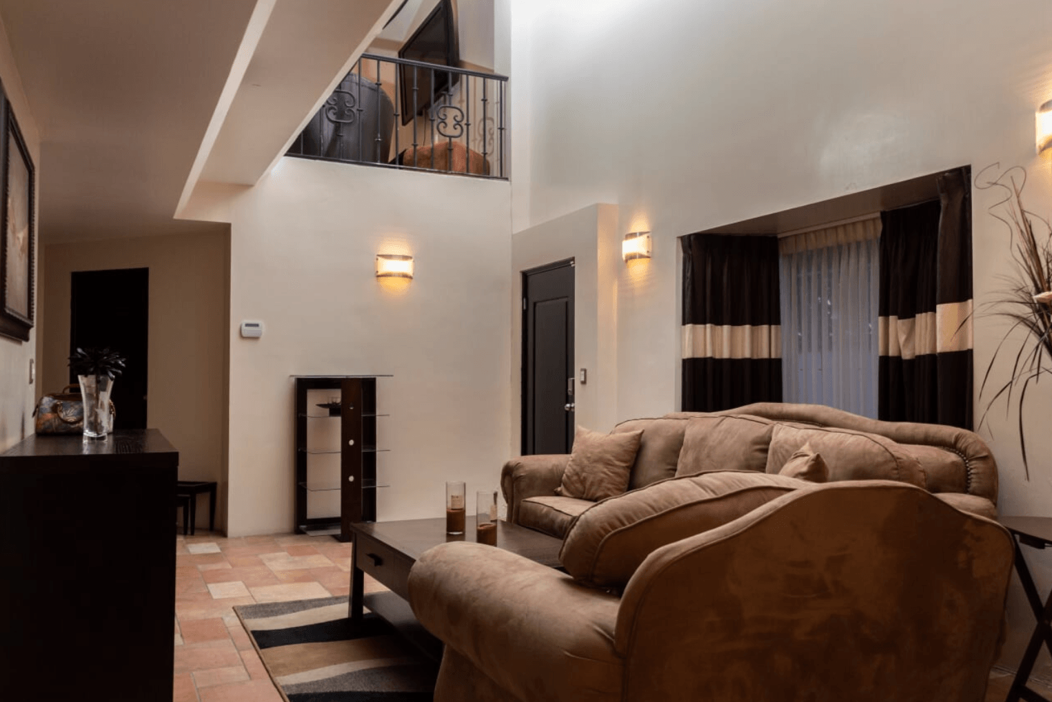 Cozy living room with beige sofa, warm wall sconces, window drapes, and a tiled floor