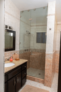 Bathroom with glass walk-in shower, dark vanity, and beige tile walls