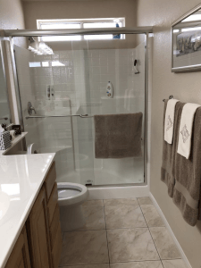 Bright bathroom with glass shower, white vanity, beige tile, and towels on wall and shower door.